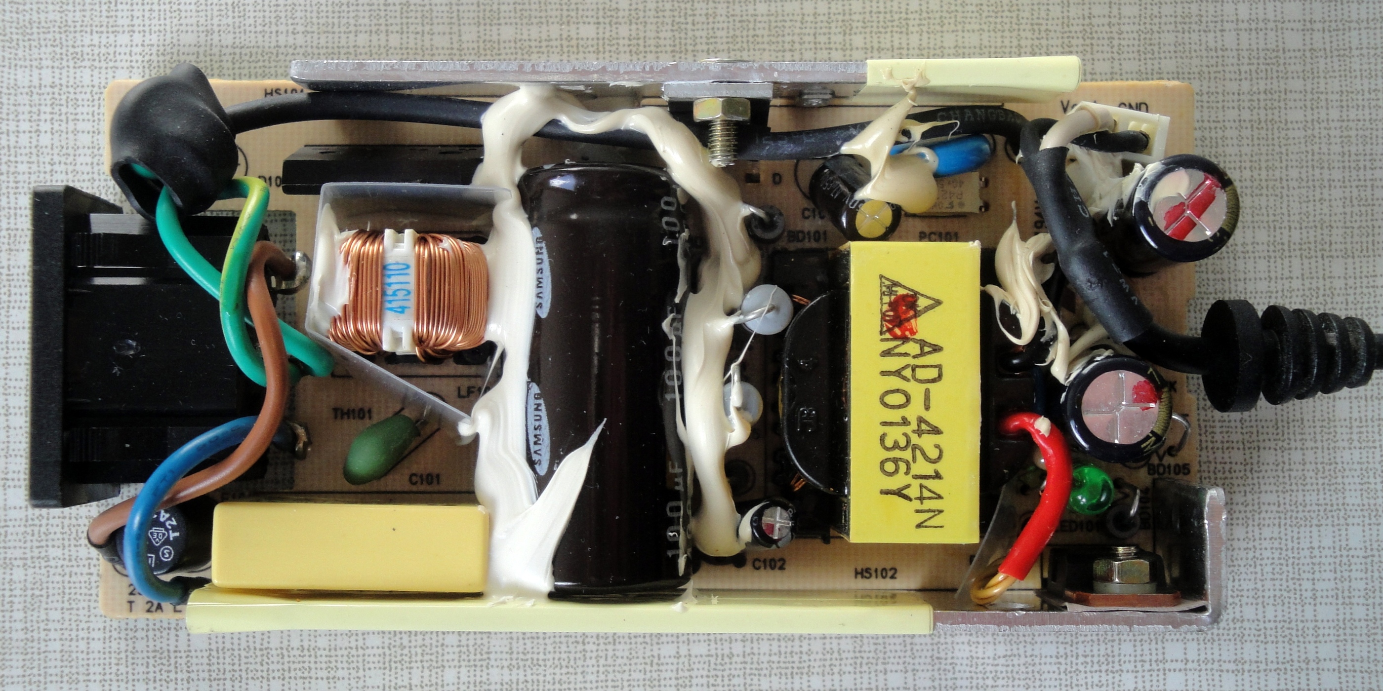 Interior photo of a disassembled silicon-era power adapter, showing a large copper-wound transformer and bulky capacitors