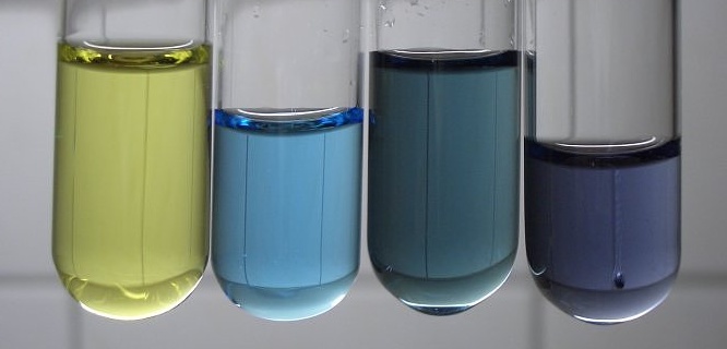 Four test tubes of vanadium electrolyte at different oxidation states, showing yellow, light blue, teal, and violet colors